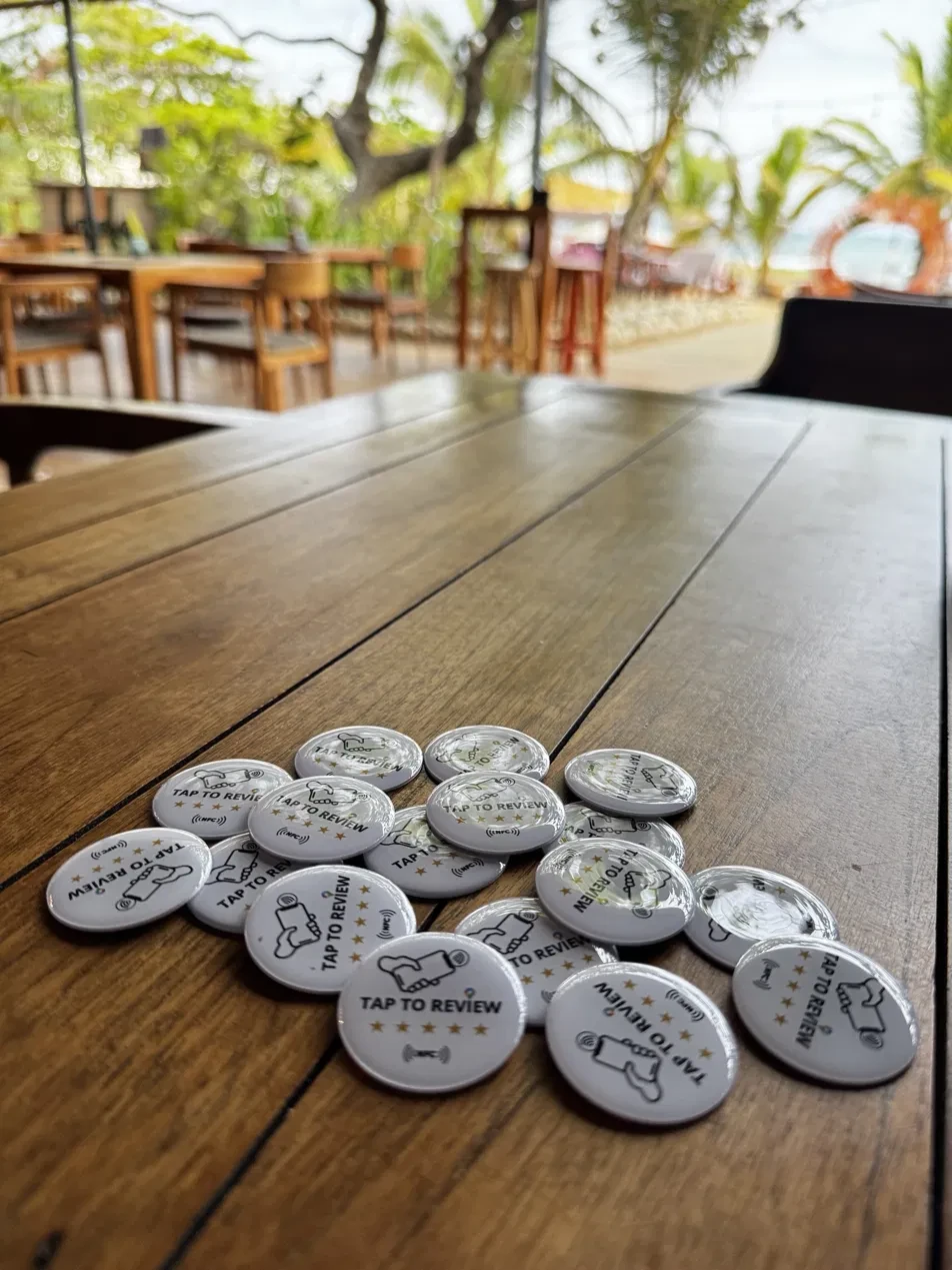 Varios stickers NFC Tap to Review sobre la mesa de madera de un restaurante frente a la playa